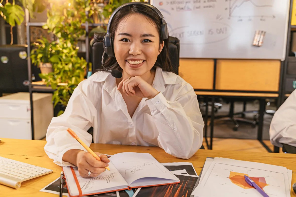 A cheerful businesswoman wearing a headset, working on documents in a modern office setting. A cheerful businesswoman wearing a headset, working on documents in a modern office setting.