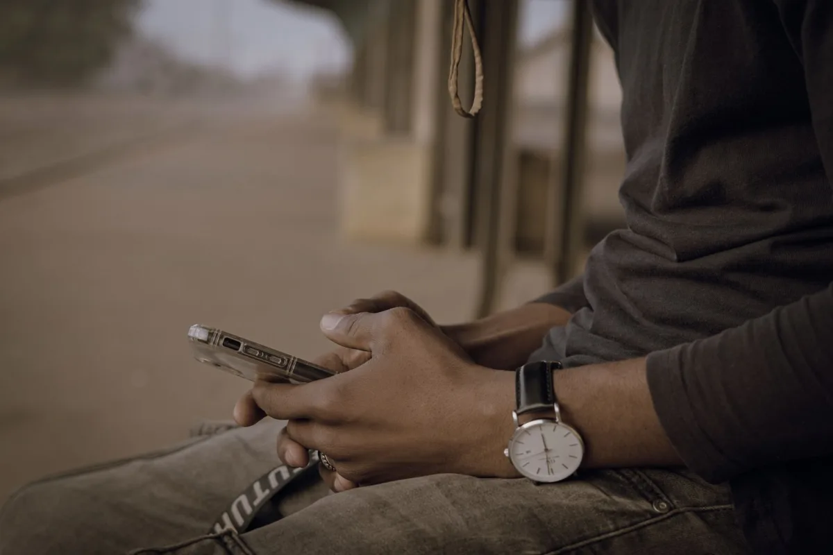 Close-up of a young man using a smartphone, sitting outdoors in Nigeria. Close-up of a young man using a smartphone, sitting outdoors in Nigeria.