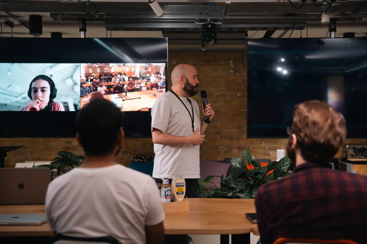 A business presentation featuring a speaker and interactive video call in an office setting. A business presentation featuring a speaker and interactive video call in an office setting.