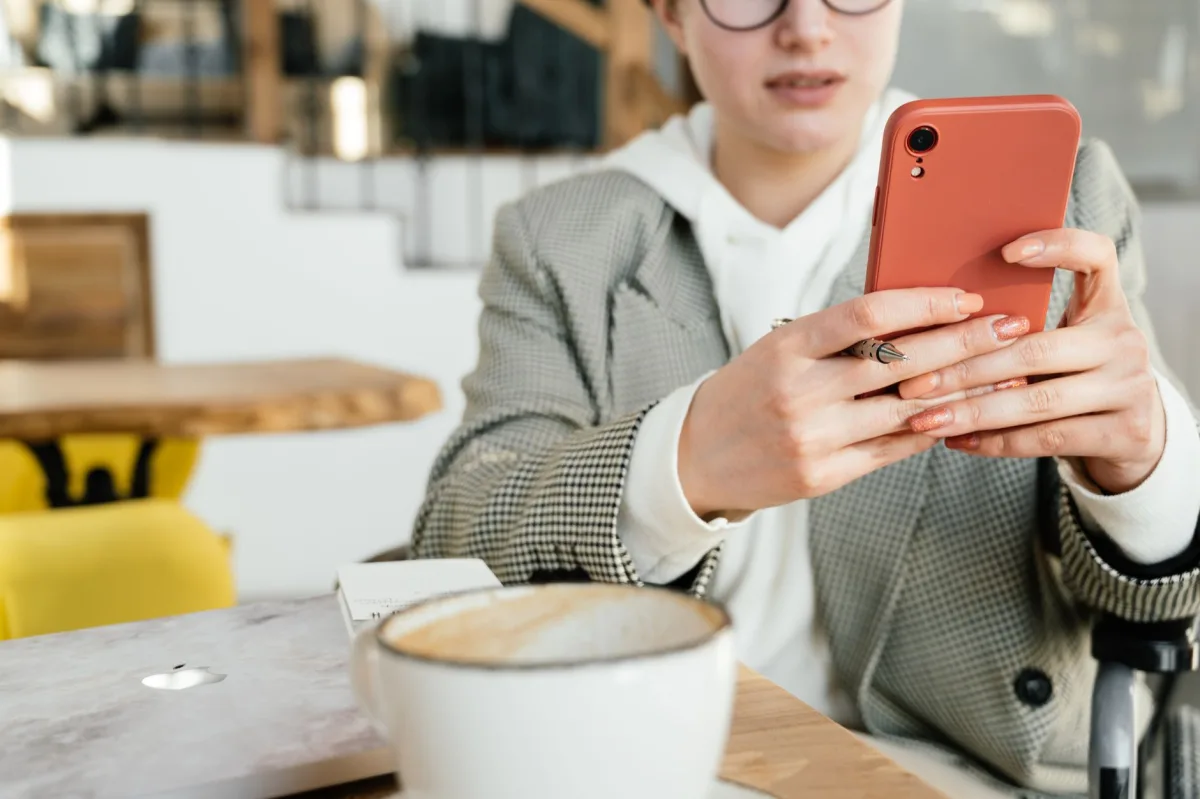 Crop focused female in formal wear and eyeglasses browsing mobile phone while having coffee in cafeteria