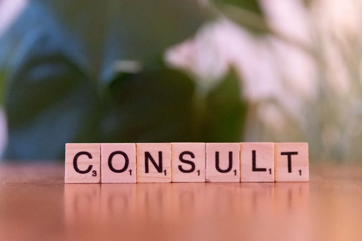 Scrabble tiles spelling 'CONSULT' on a wooden table with blurred background. Scrabble tiles spelling 'CONSULT' on a wooden table with blurred background.