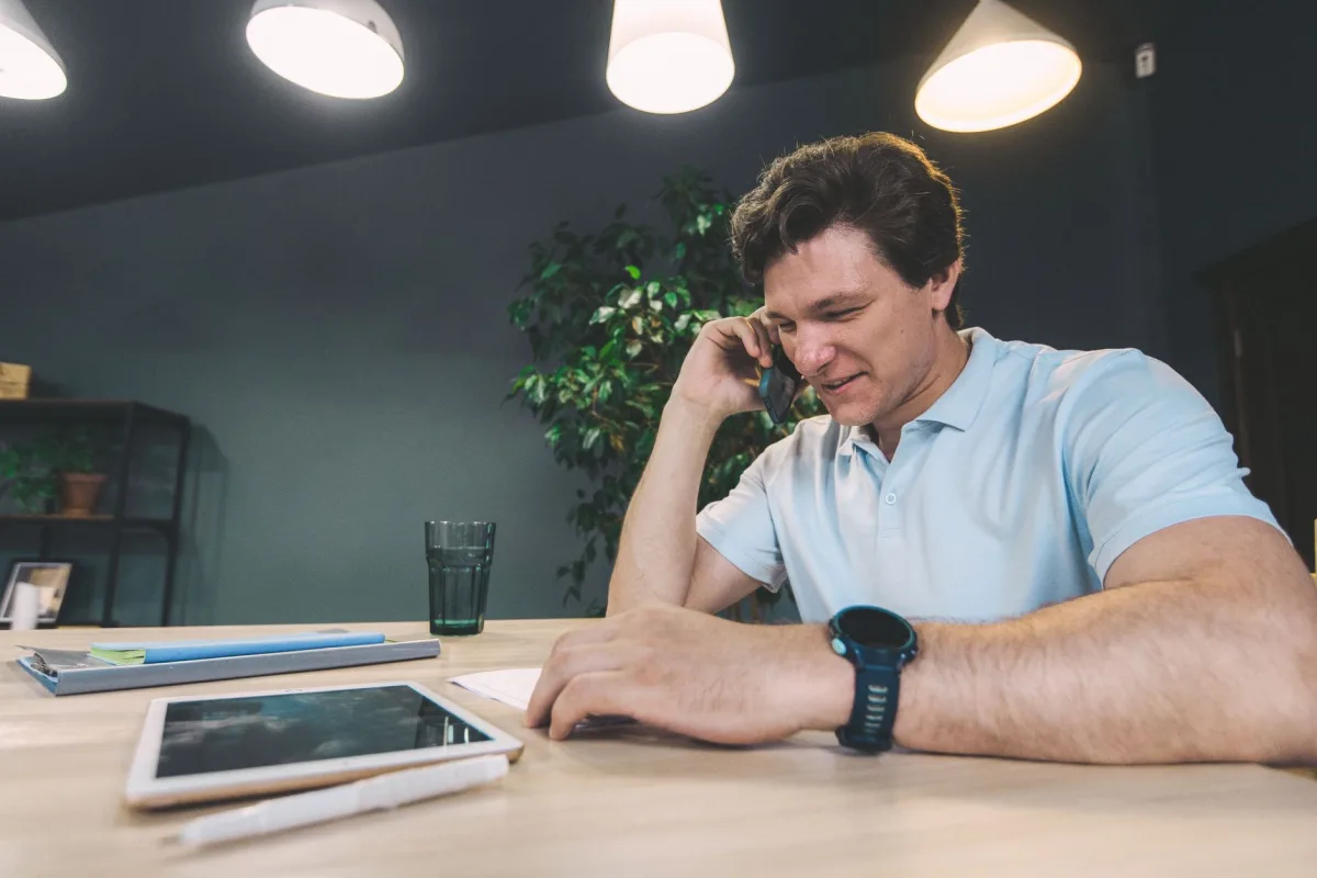 Businessman at a desk using a smartphone with a tablet, emphasizing connectivity. Businessman at a desk using a smartphone with a tablet, emphasizing connectivity.