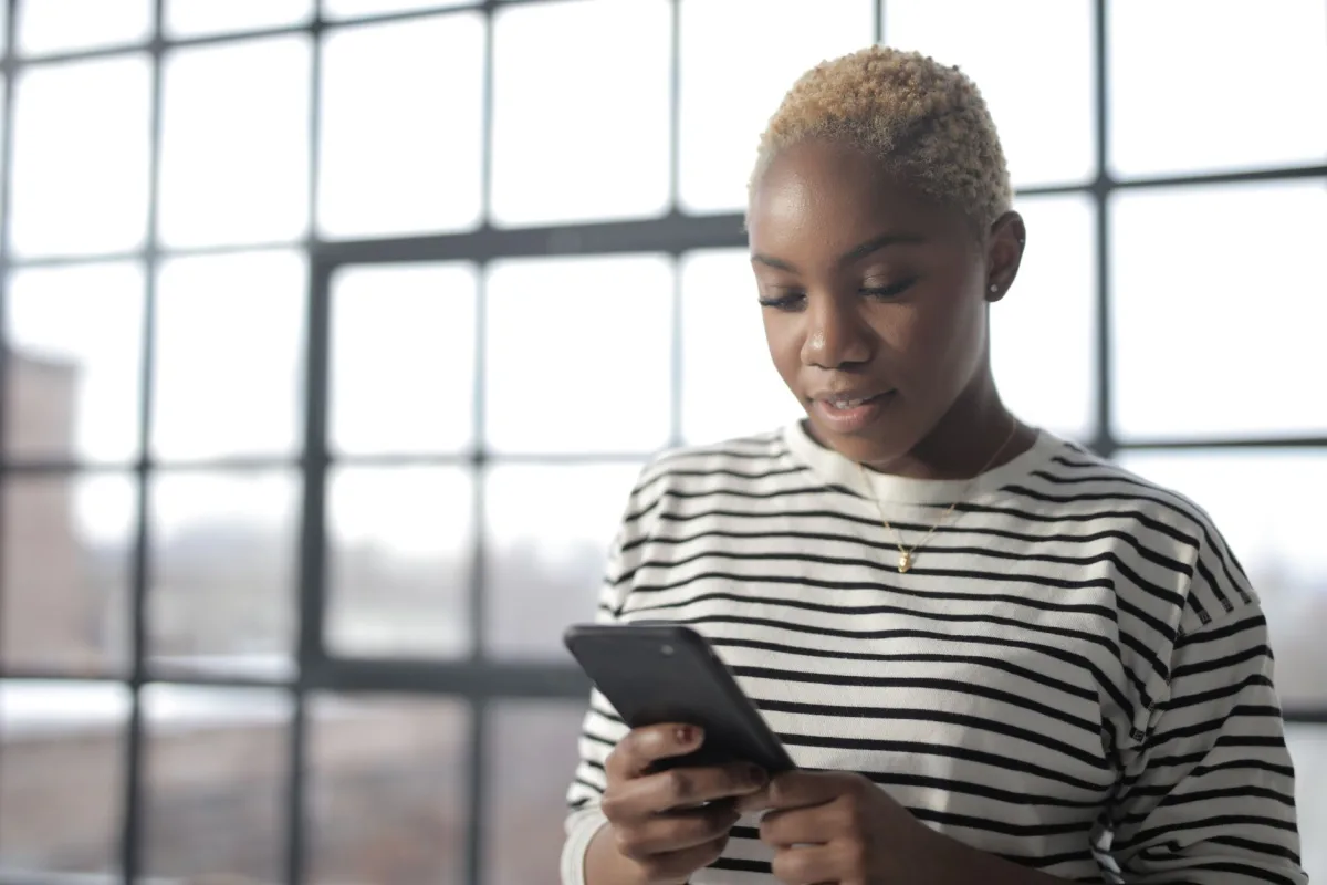Young African American woman texting on smartphone by a window with natural light. Young African American woman texting on smartphone by a window with natural light.