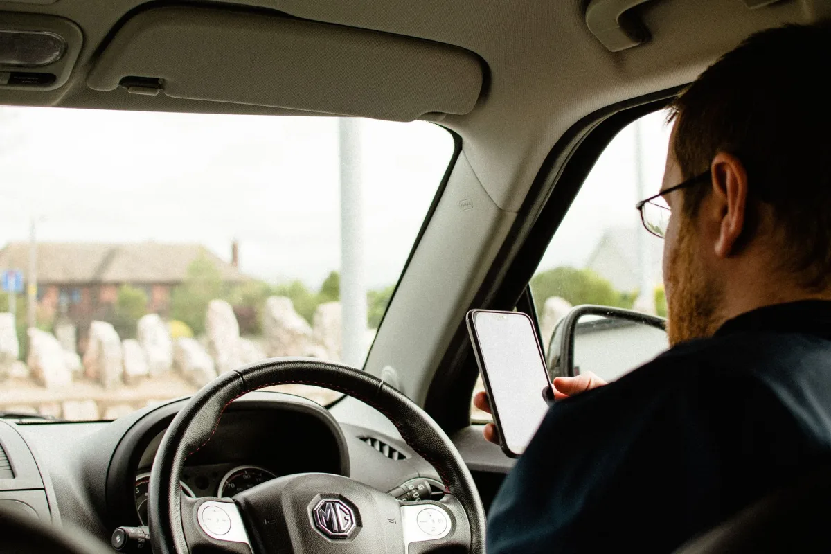 Back view of anonymous male in casual clothes sitting in car behind wheel and using smartphone
