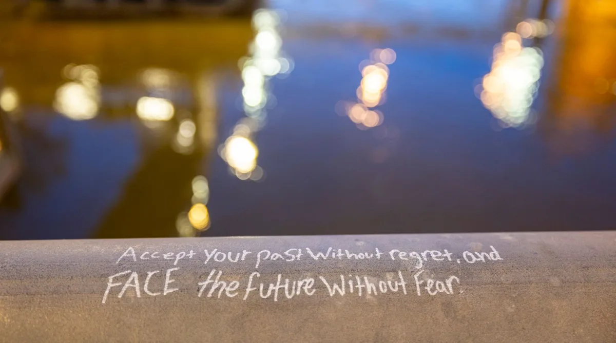 A motivational quote on a railing, reflecting city lights in the water.