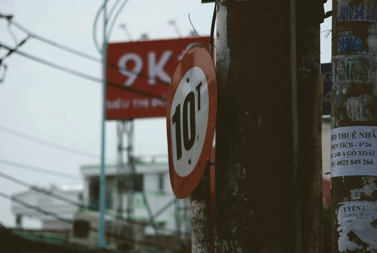 Urban street scene featuring a weathered 10t weight limit sign, with wires and poles.