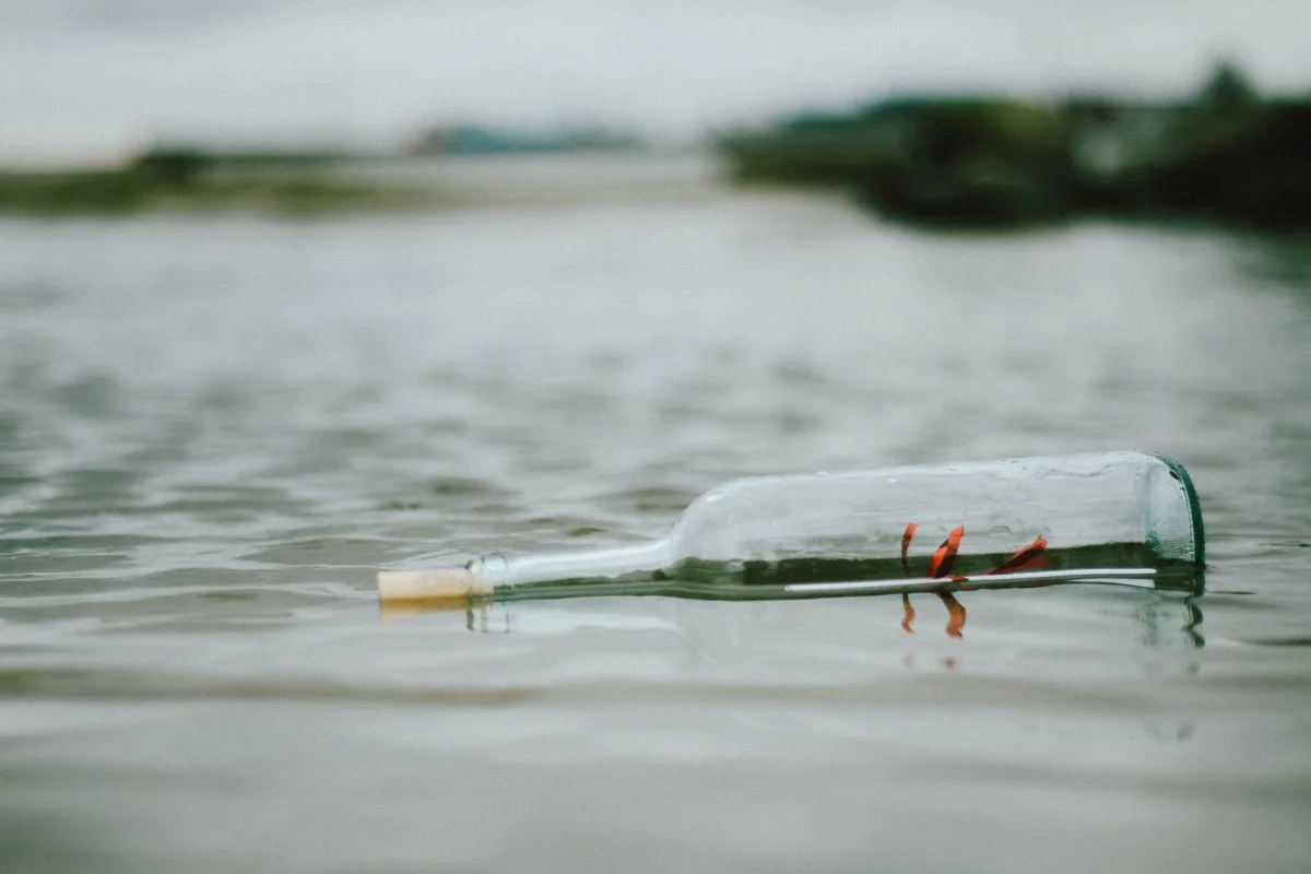 A glass bottle with a letter inside floats on a tranquil water surface, creating a sense mystery.