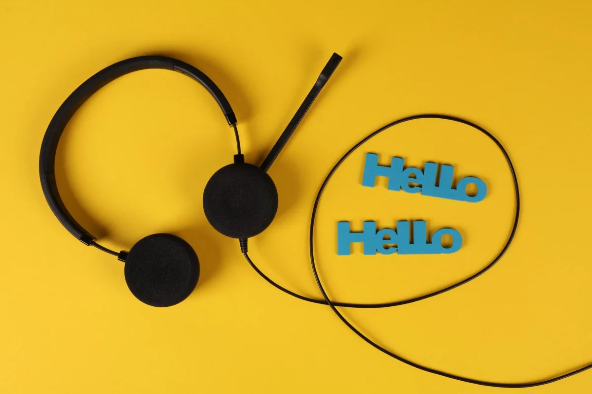 Top view of black headset with 'Hello' text on a bright yellow background, illustrating technology and communication concepts. Top view of black headset with 'Hello' text on a bright yellow background, illustrating technology and communication concepts.