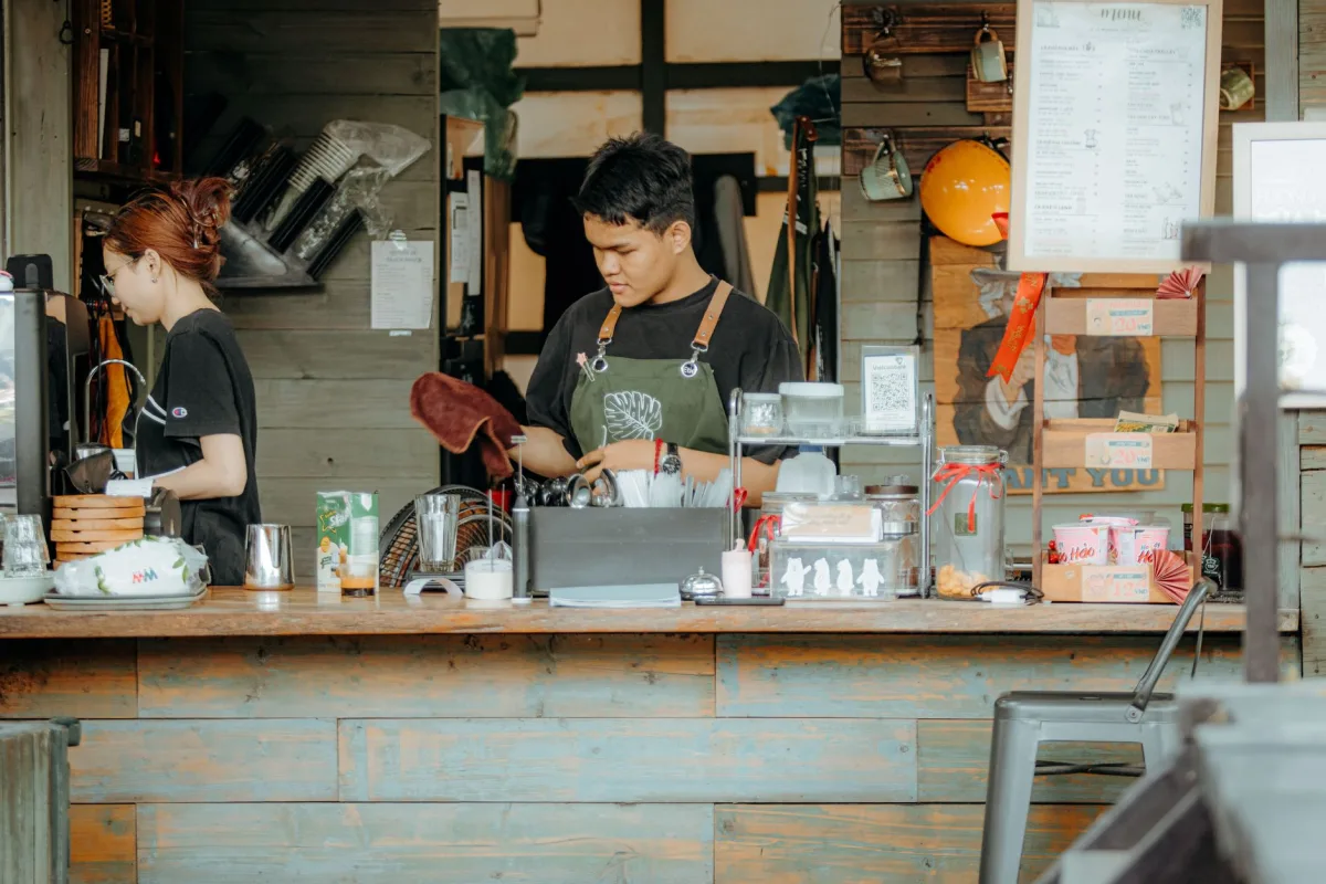 Two baristas working in a cozy coffee shop setting, preparing drinks and engaging with customers.