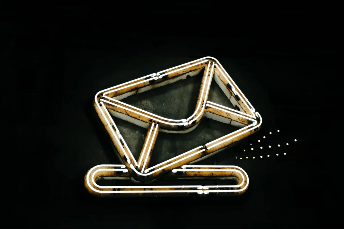 A glowing neon envelope symbol against a black background, conveying messaging or email concept. A glowing neon envelope symbol against a black background, conveying messaging or email concept.
