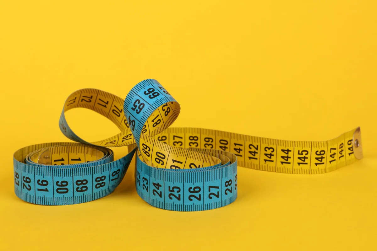 A coiled blue and yellow measuring tape on a bright yellow background. A coiled blue and yellow measuring tape on a bright yellow background.