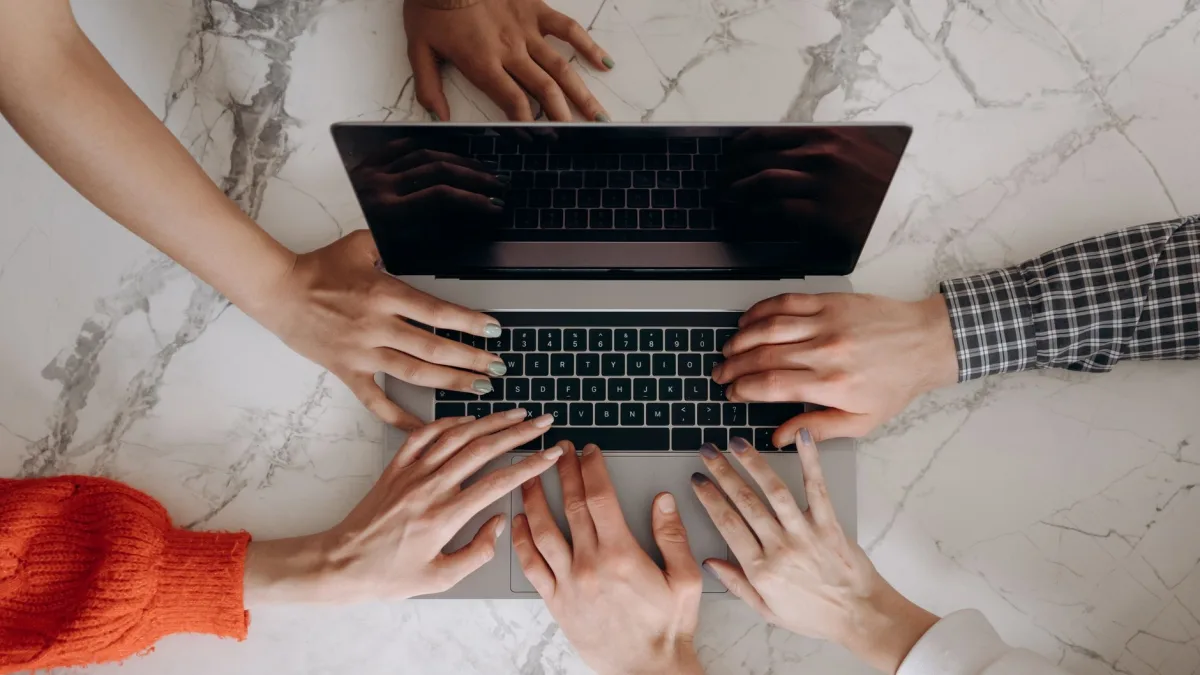 Top view of multiple hands working together on a laptop keyboard, symbolizing teamwork. Top view of multiple hands working together on a laptop keyboard, symbolizing teamwork.