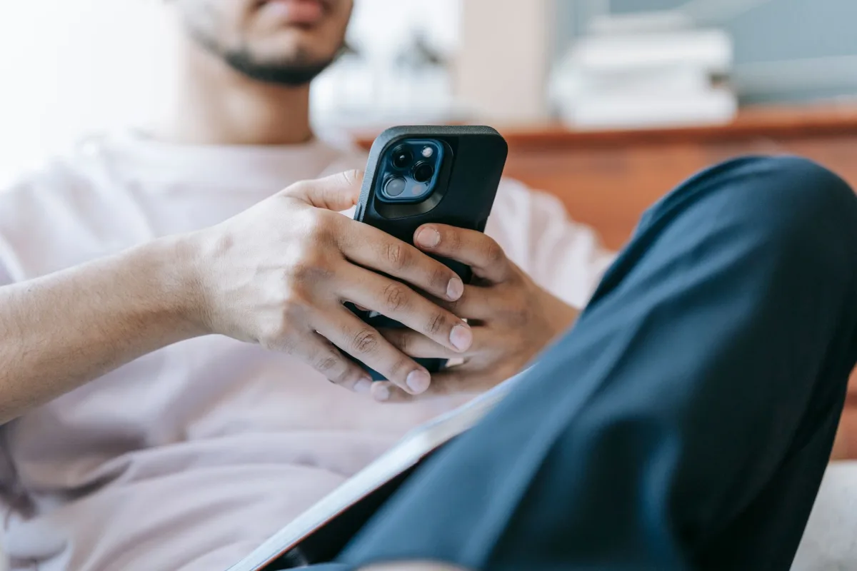 Crop bearded male in casual clothes browsing mobile phone and sitting in light living room Crop bearded male in casual clothes browsing mobile phone and sitting in light living room