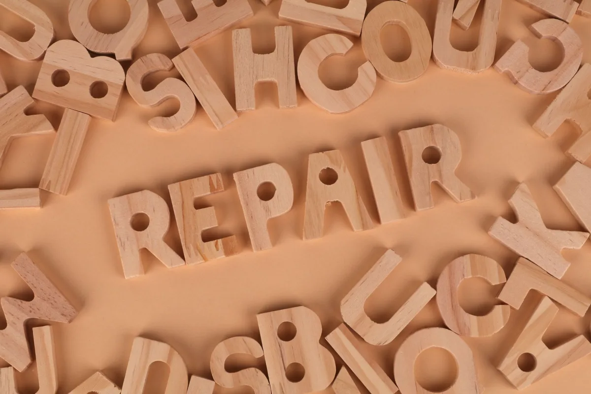 Top view of wooden letters arranged to spell 'REPAIR' on a beige background, perfect for DIY themes.
