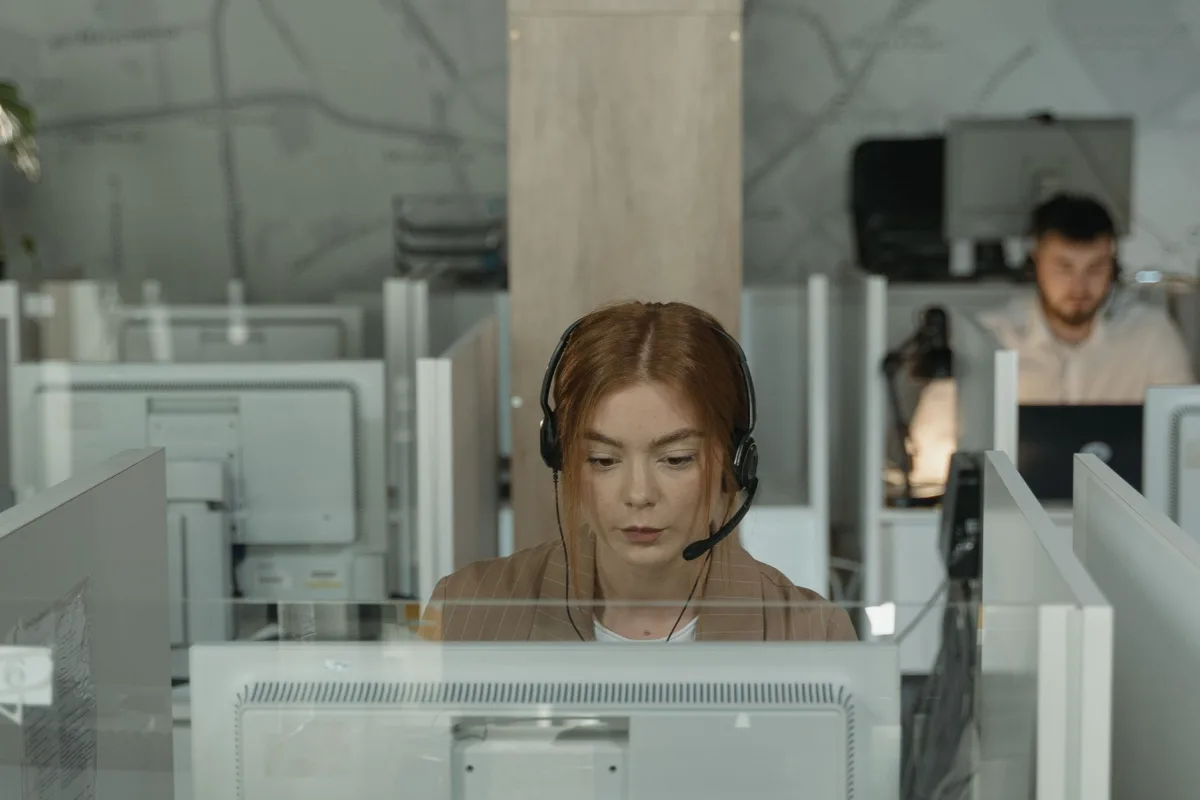 Focused call center agent wearing headset working in cubicle office space Focused call center agent wearing headset working in cubicle office space