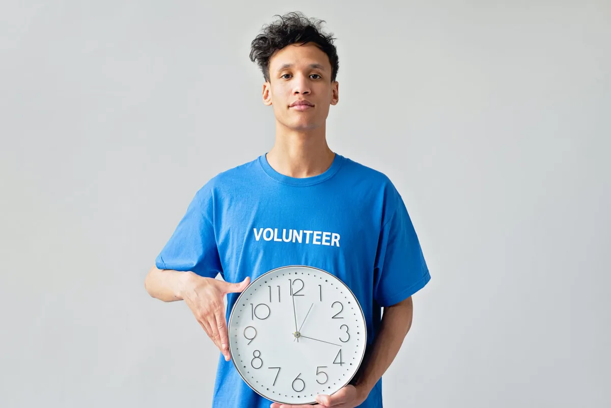 Young male volunteer in blue shirt holding a clock, symbolizing management.