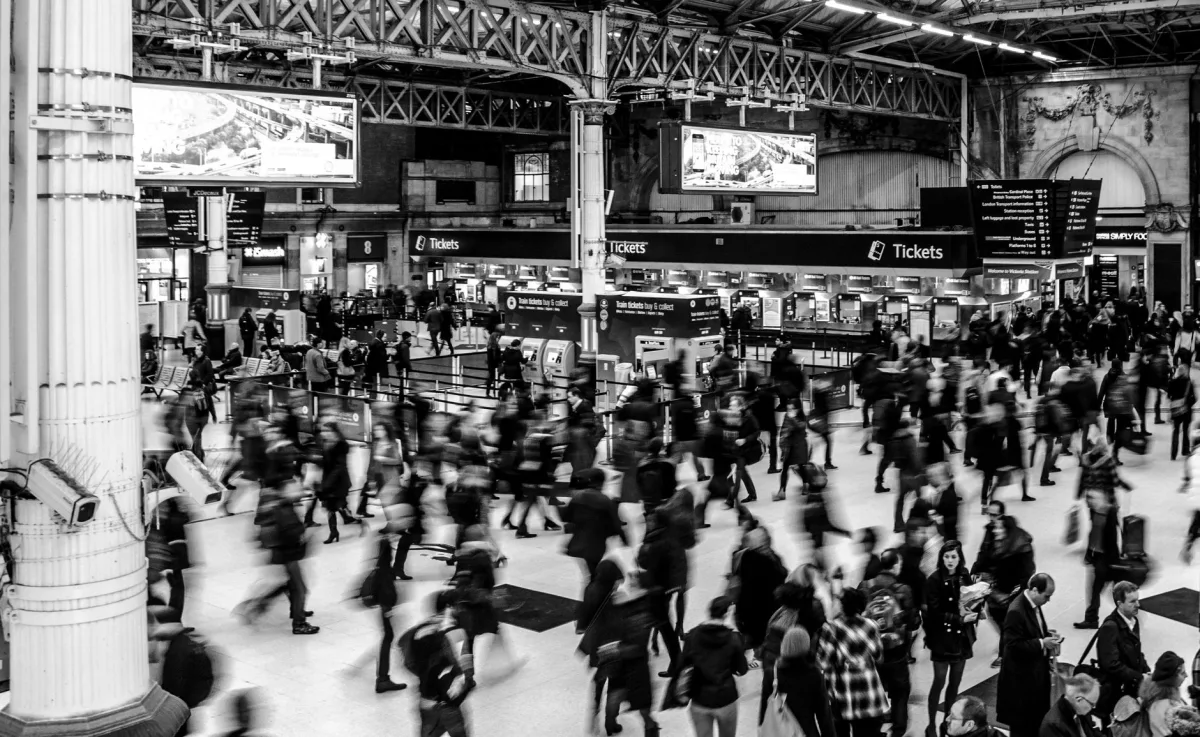 Dynamic black and white image capturing a busy train station with a crowd of commuters.