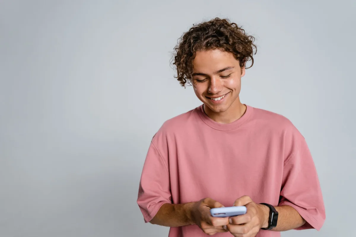 Teenager with curly hair smiling down at smartphone in a studio setup. Teenager with curly hair smiling down at smartphone in a studio setup.
