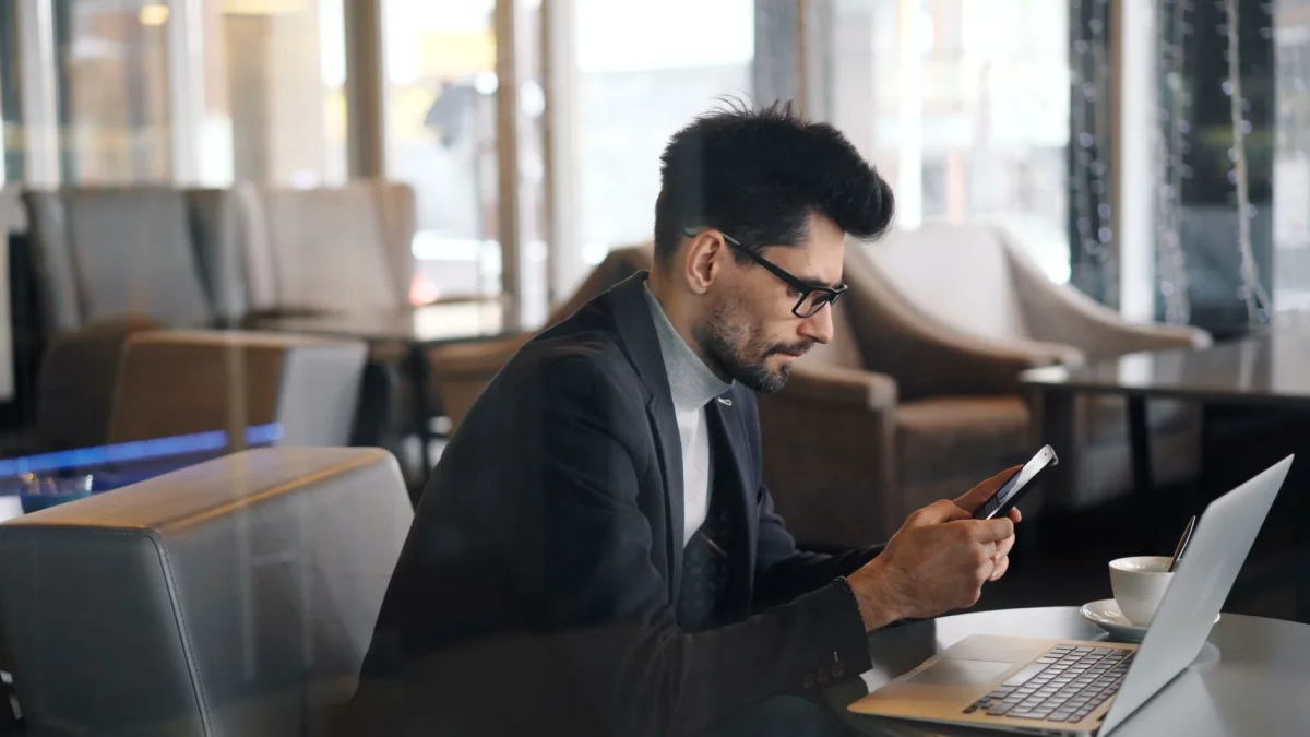 Confident businessman using smartphone in a modern café setting. Confident businessman using smartphone in a modern café setting.