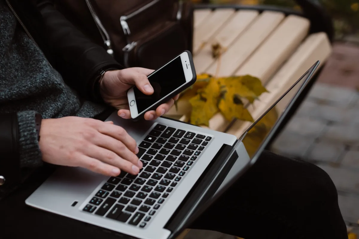 Person working remotely using a laptop and smartphone outdoors, embodying digital nomad lifestyle.