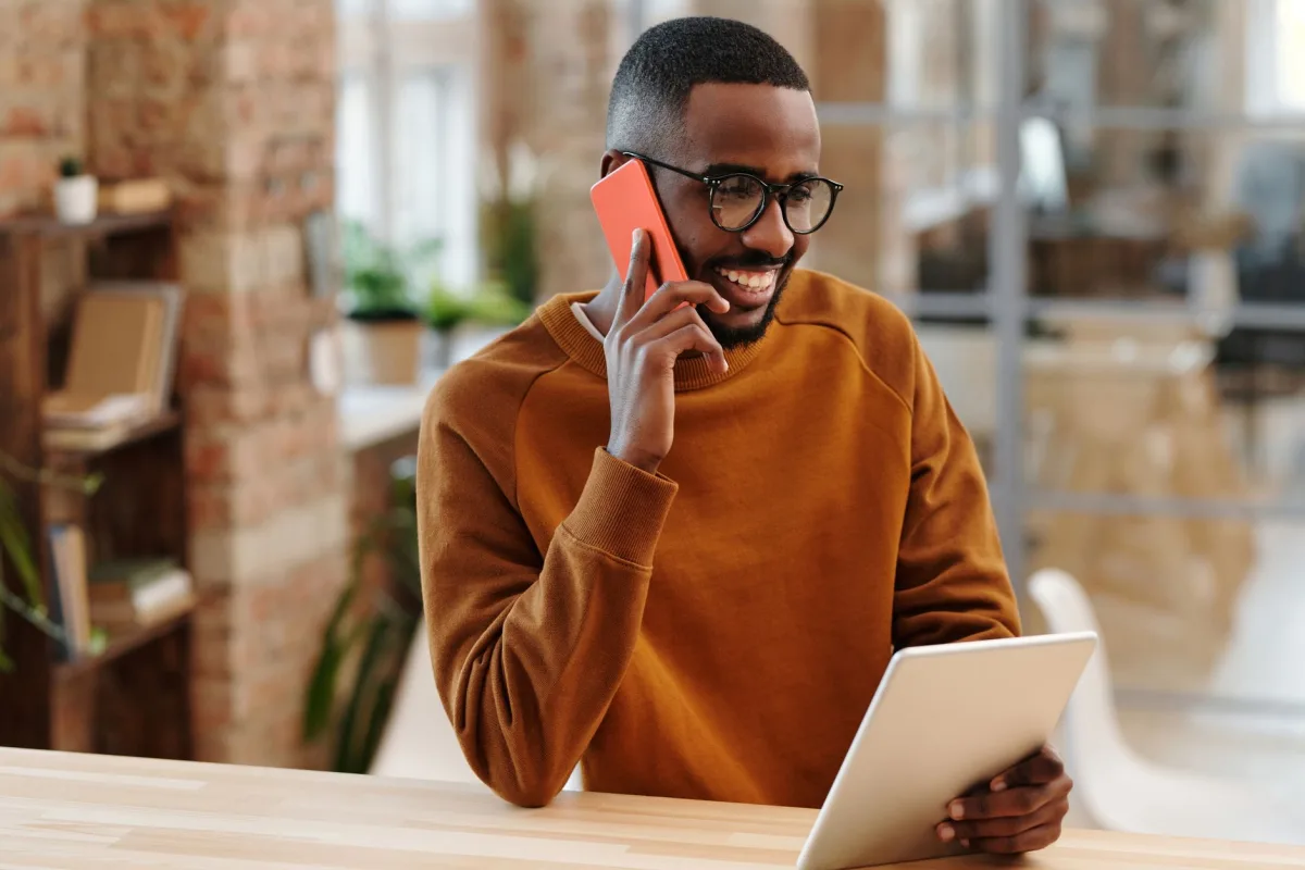 Smiling man in an office multitasking with a phone and digital tablet. Smiling man in an office multitasking with a phone and digital tablet.