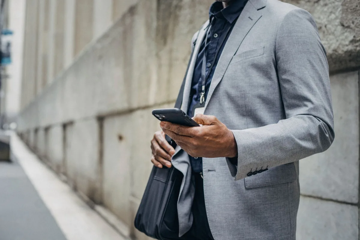 Crop unrecognizable African American male in formal suit standing on street and browsing modern mobile phone Crop unrecognizable African American male in formal suit standing on street and browsing modern mobile phone