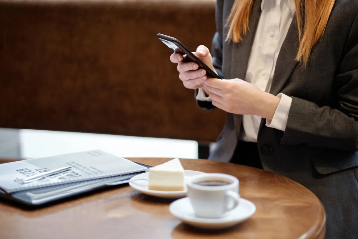 Businesswoman in cafe using smartphone, enjoying coffee and cake during break.