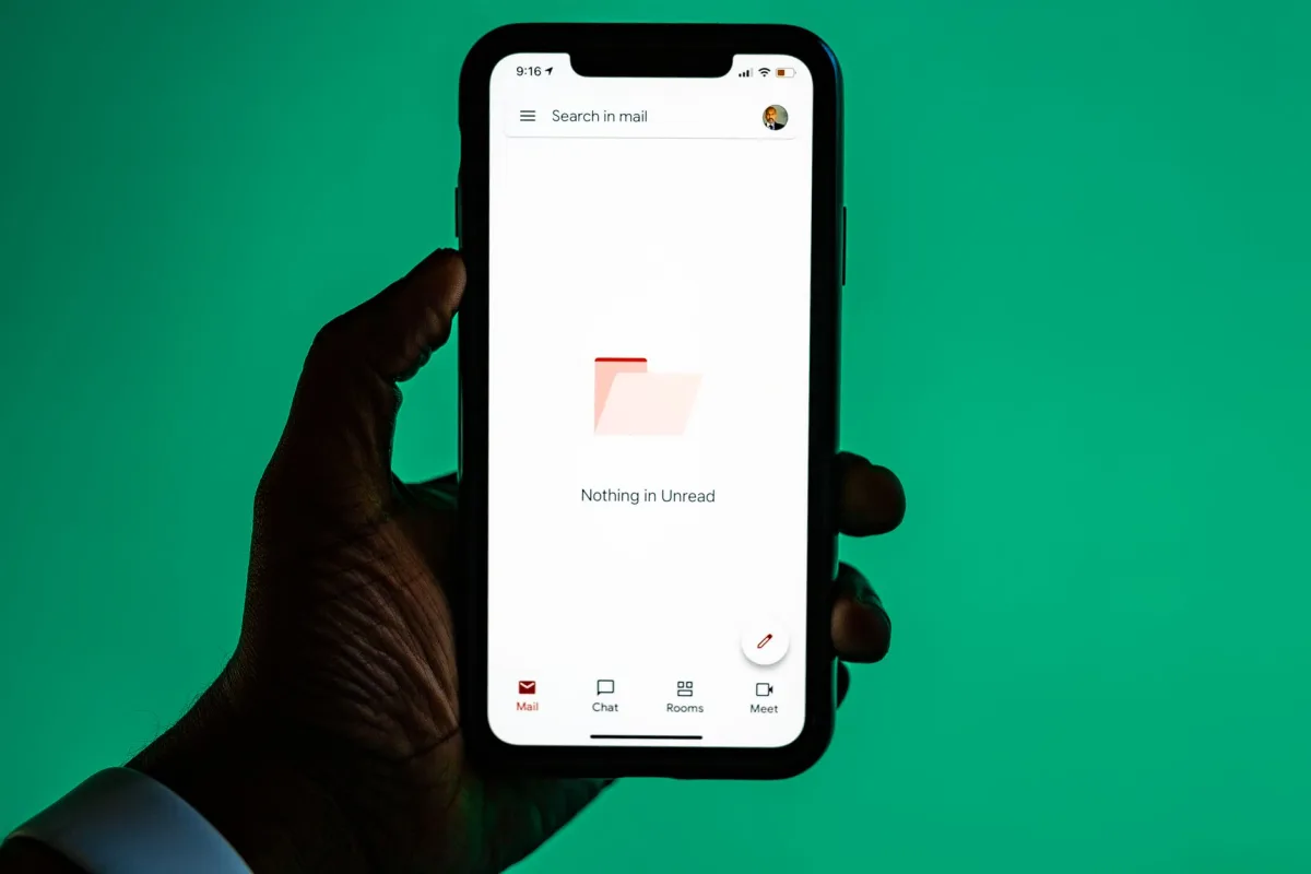 Close-up of a hand holding a smartphone displaying email app against a green background. Close-up of a hand holding a smartphone displaying email app against a green background.