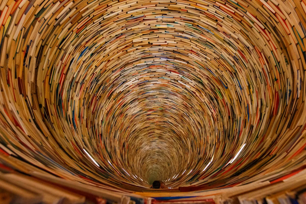 An artistic spiral tunnel made entirely of stacked books creating an intriguing vortex effect. An artistic spiral tunnel made entirely of stacked books creating an intriguing vortex effect.