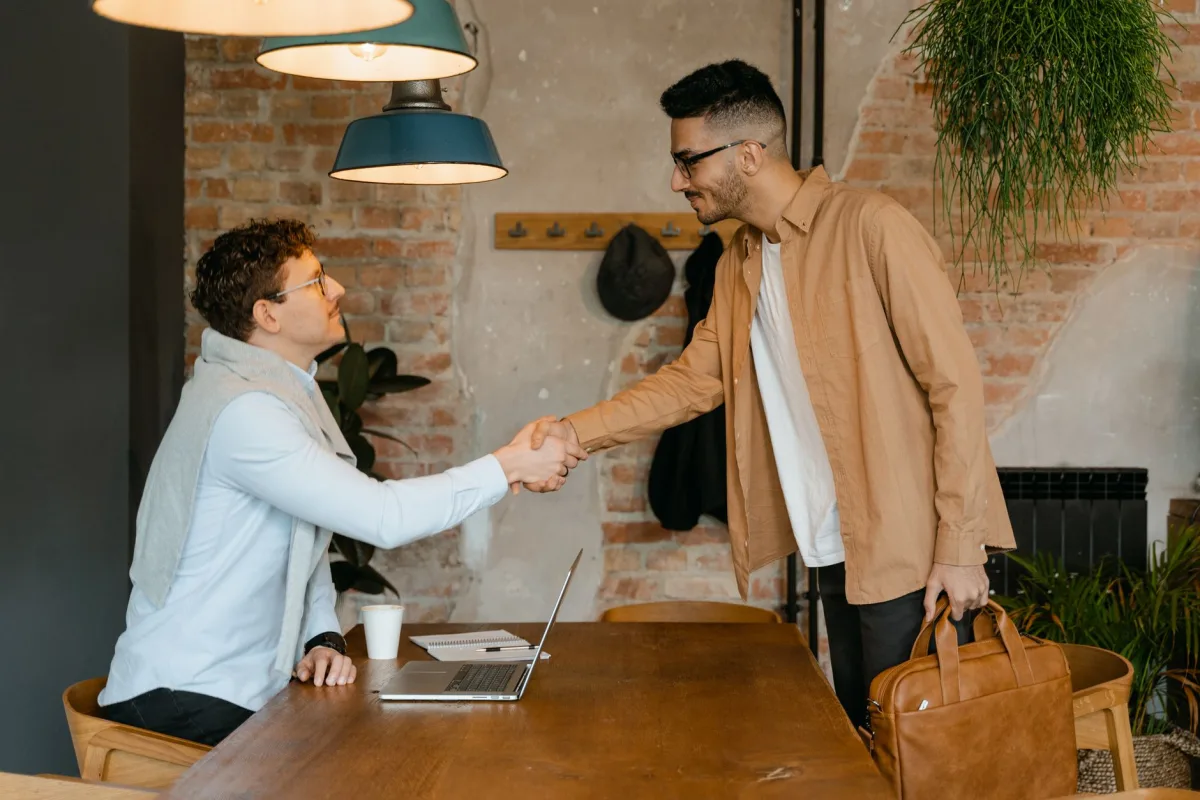 Two businessmen shake hands in a modern office setting, sealing a partnership.