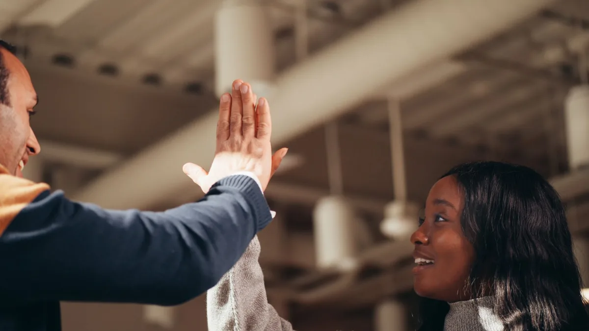 Two colleagues celebrating success with a high five in an office setting.