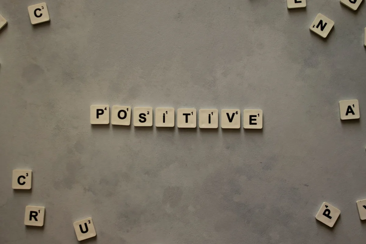 Scrabble tiles arranged to spell 'positive' on gray textured surface, conveying optimism.