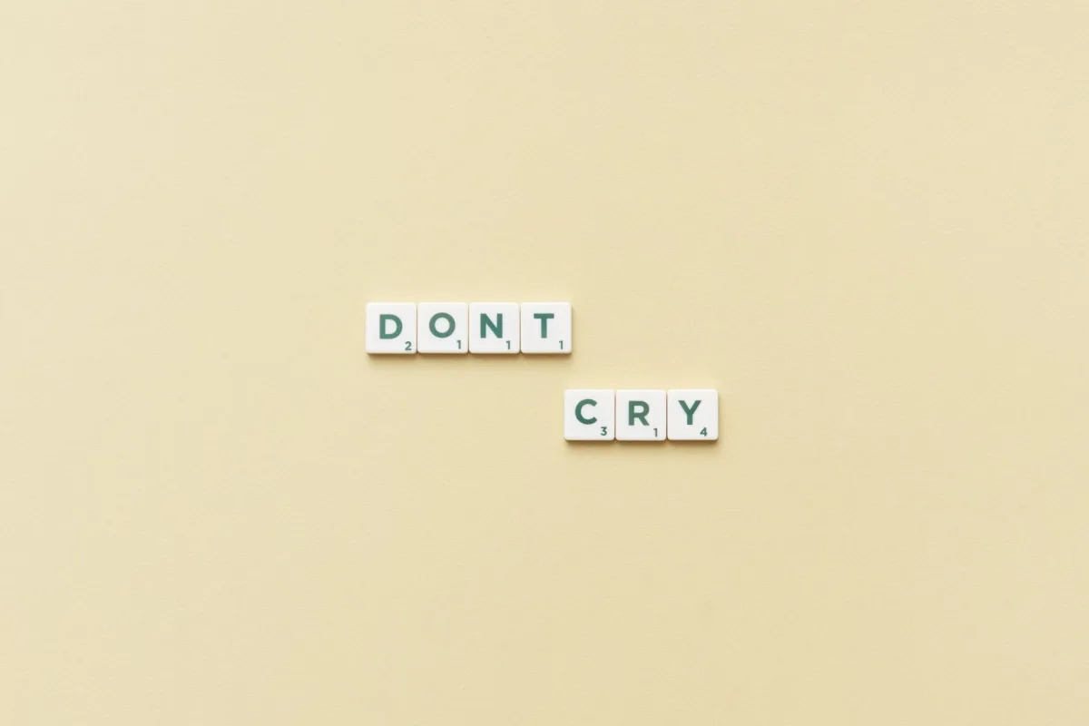 Scrabble tiles forming the phrase 'Don't Cry' on a simple yellow background, top view. Scrabble tiles forming the phrase 'Don't Cry' on a simple yellow background, top view.