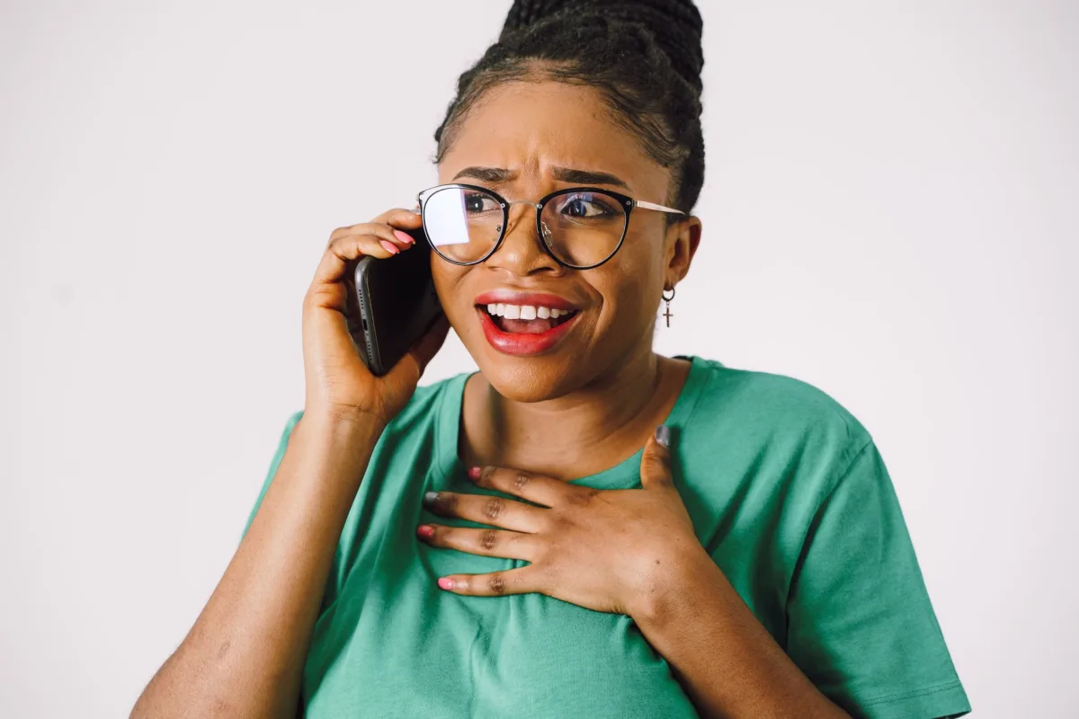 A surprised woman with eyeglasses talks on a smartphone, expressing emotion.