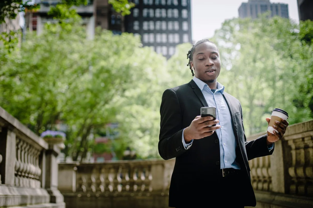 Low angle of happy young African American male suit reading good news on cellphone during coffee break downtown