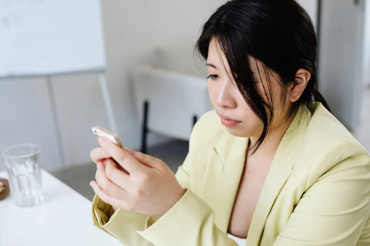 Focused woman yellow blazer texting on smartphone at the office table.
