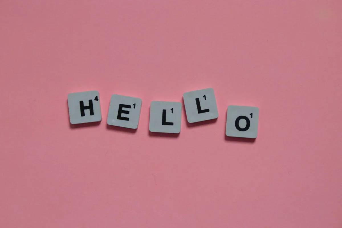 Scrabble tiles arranged to spell 'hello' on a soft pink background, with copy space.