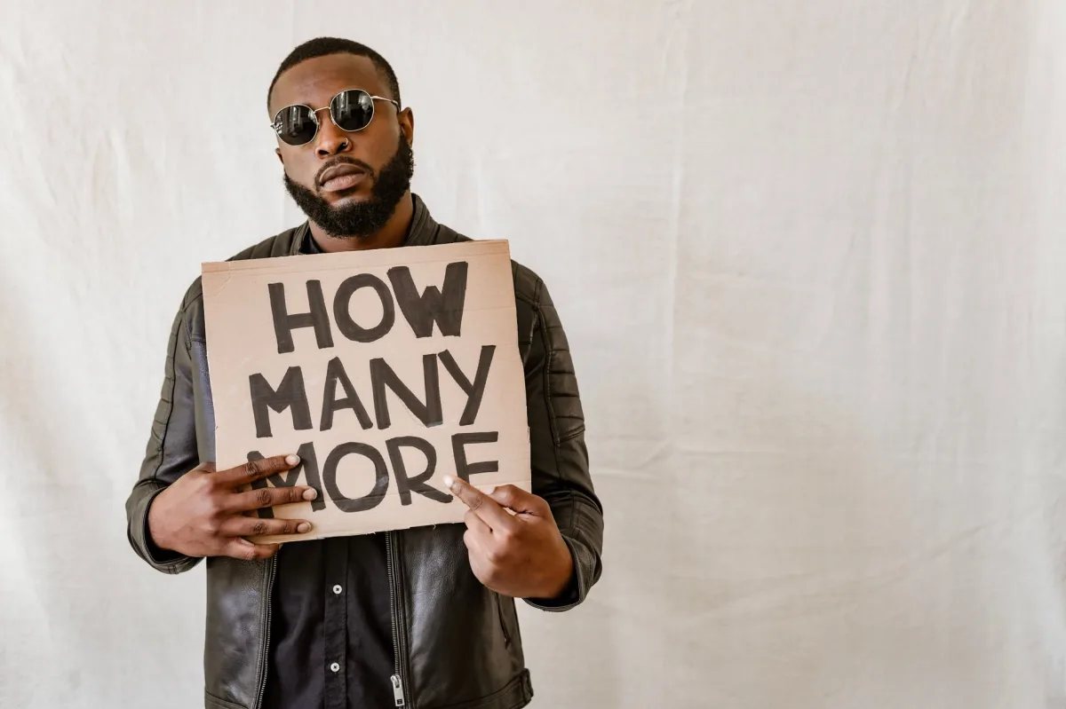 Man holding cardboard sign with 'How Many More' on a neutral background. Man holding cardboard sign with 'How Many More' on a neutral background.