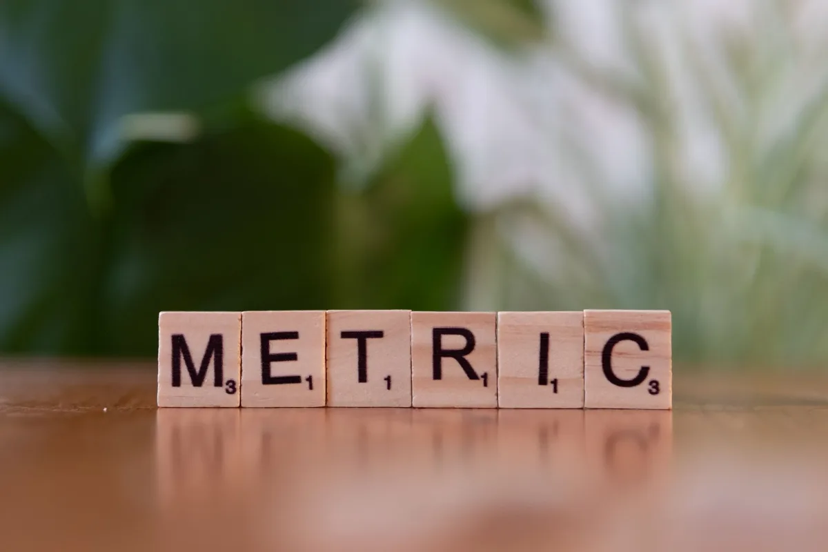 Close-up wooden tiles spelling 'Metric' on a table, with a blurred green background. Close-up wooden tiles spelling 'Metric' on a table, with a blurred green background.
