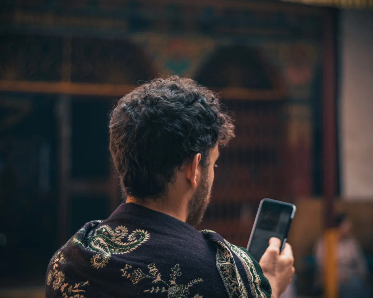 A person views their smartphone while wearing a detailed shawl, focusing on technology and culture.