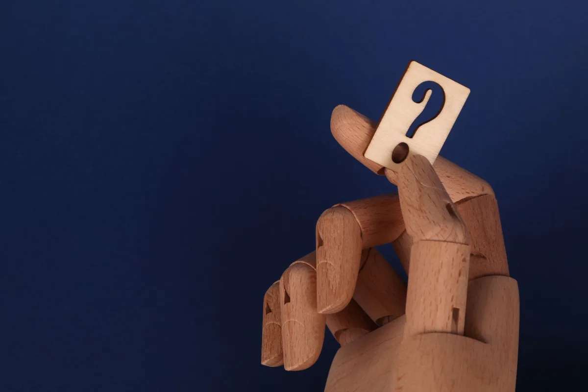 Wooden mannequin hand holding a block with a question mark against a blue background. Wooden mannequin hand holding a block with a question mark against a blue background.