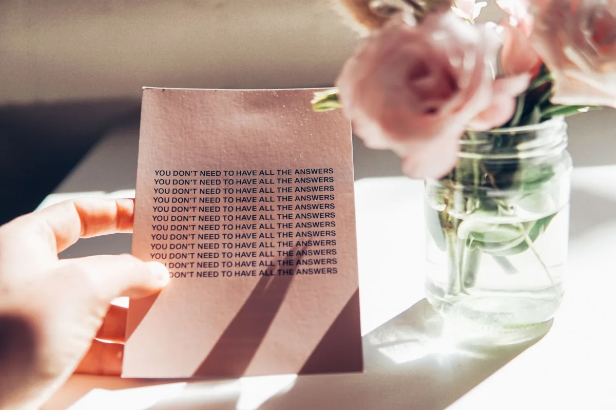 A calming card with a motivational quote beside pink flowers in a sunlit interior. A calming card with a motivational quote beside pink flowers in a sunlit interior.