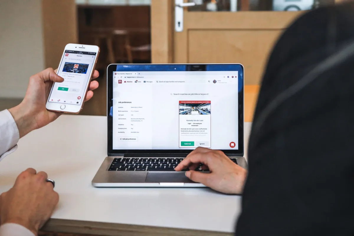 Hands using smartphone and laptop digital browsing in an office setting, showcasing remote work culture.