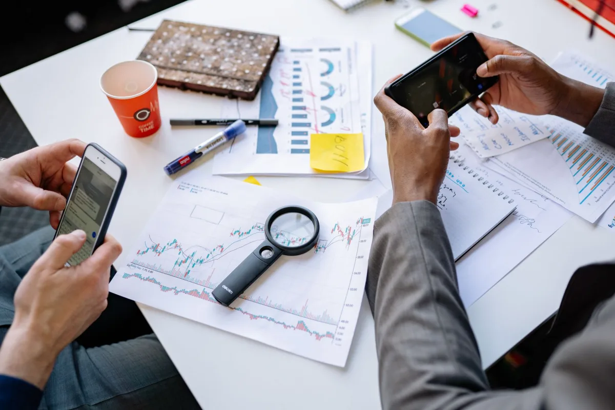 Two professionals analyzing and graphs with smartphones on a white table. Two professionals analyzing and graphs with smartphones on a white table.