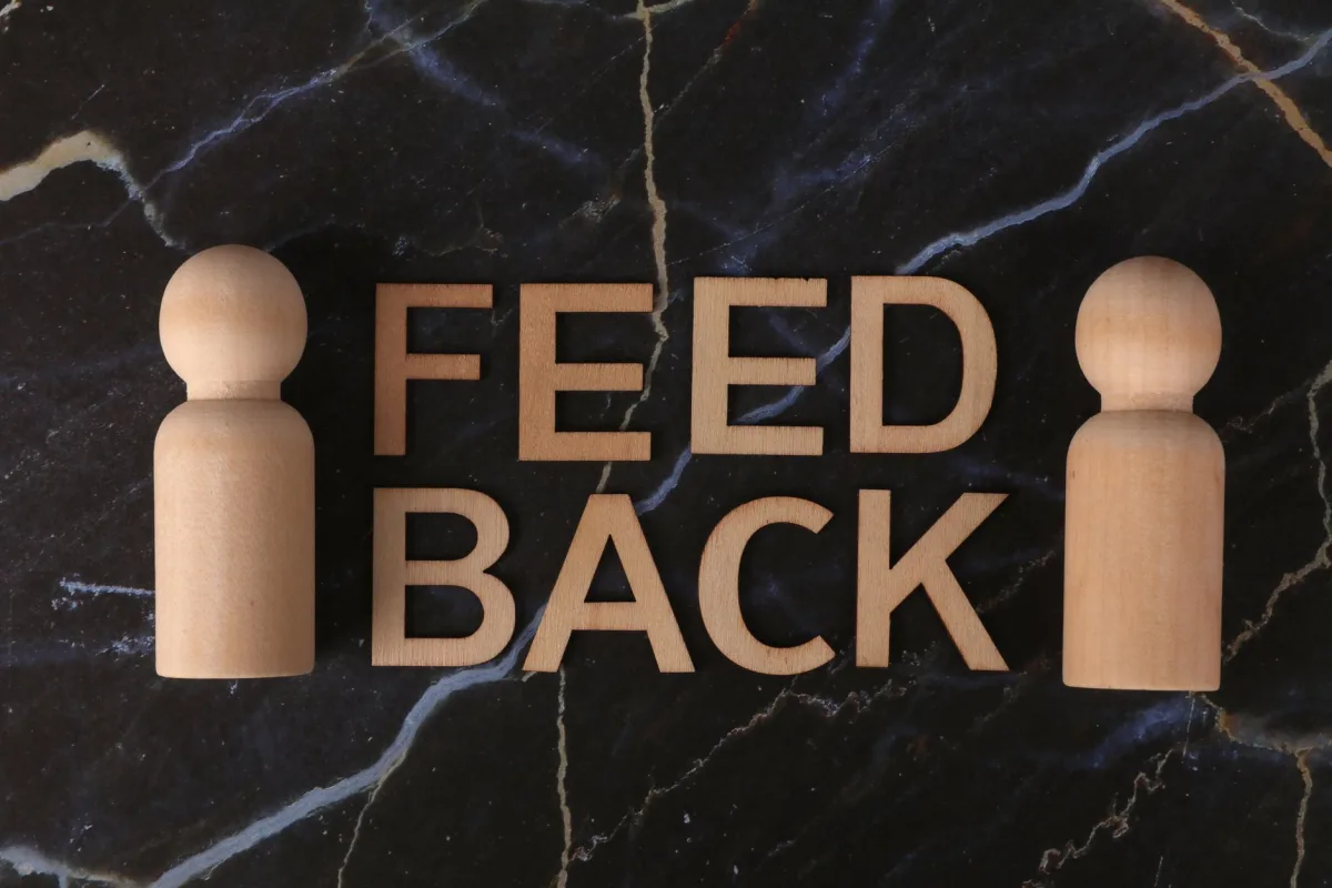 Wooden letters spelling 'Feedback' with peg-like figures on marble background. Wooden letters spelling 'Feedback' with peg-like figures on marble background.