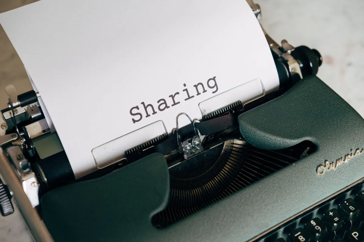 Close-up of a vintage typewriter with paper showing the word 'Sharing', conveying retro