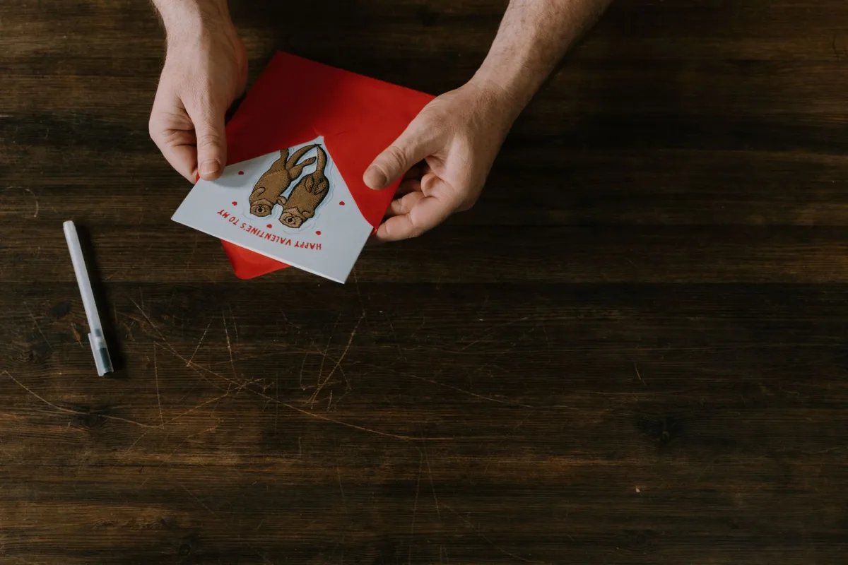 Hands holding a Valentine's Day card with a red envelope on a dark wooden table. Hands holding a Valentine's Day card with a red envelope on a dark wooden table.