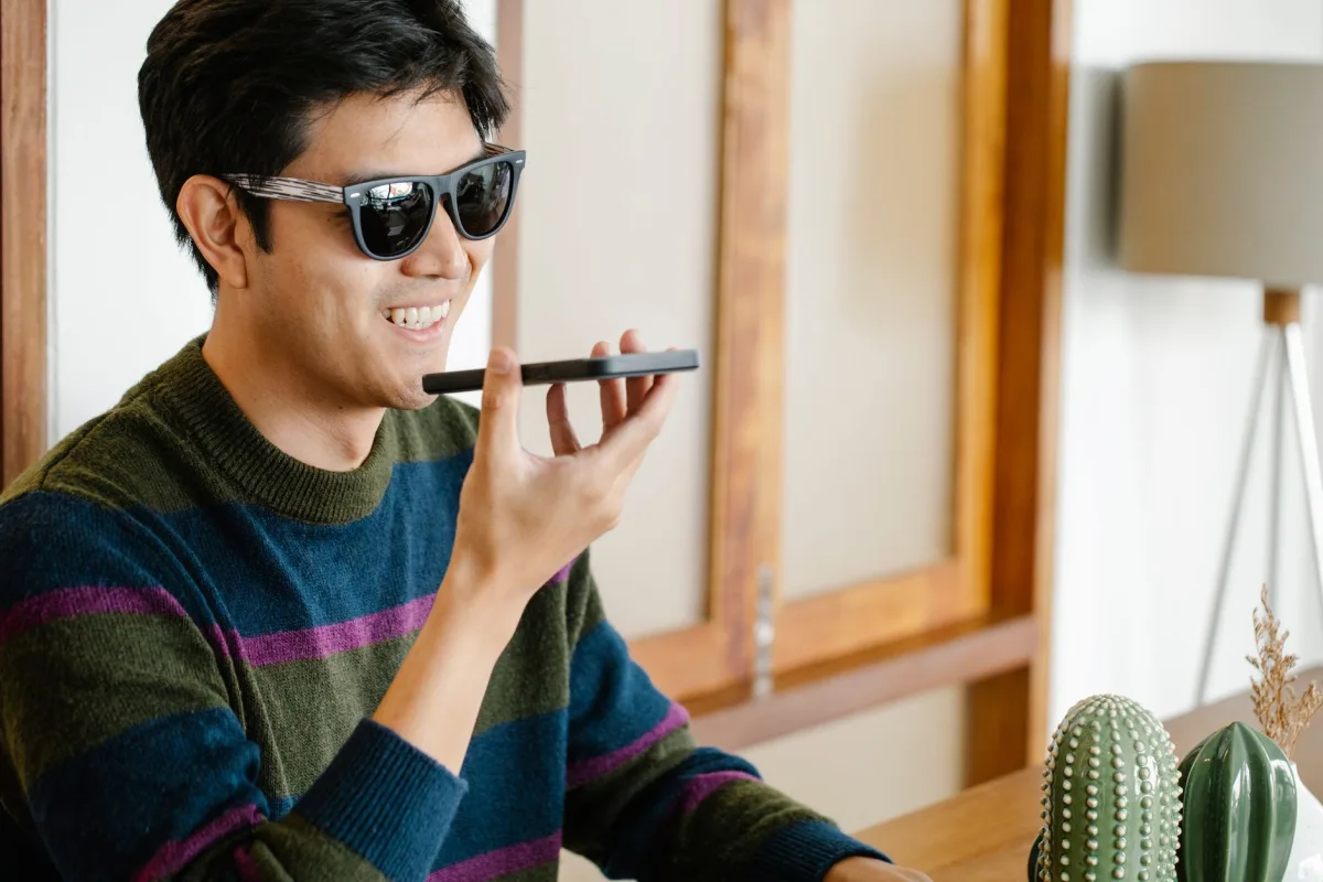 Young man wearing sunglasses smiles while using features on his smartphone indoors. Young man wearing sunglasses smiles while using features on his smartphone indoors.