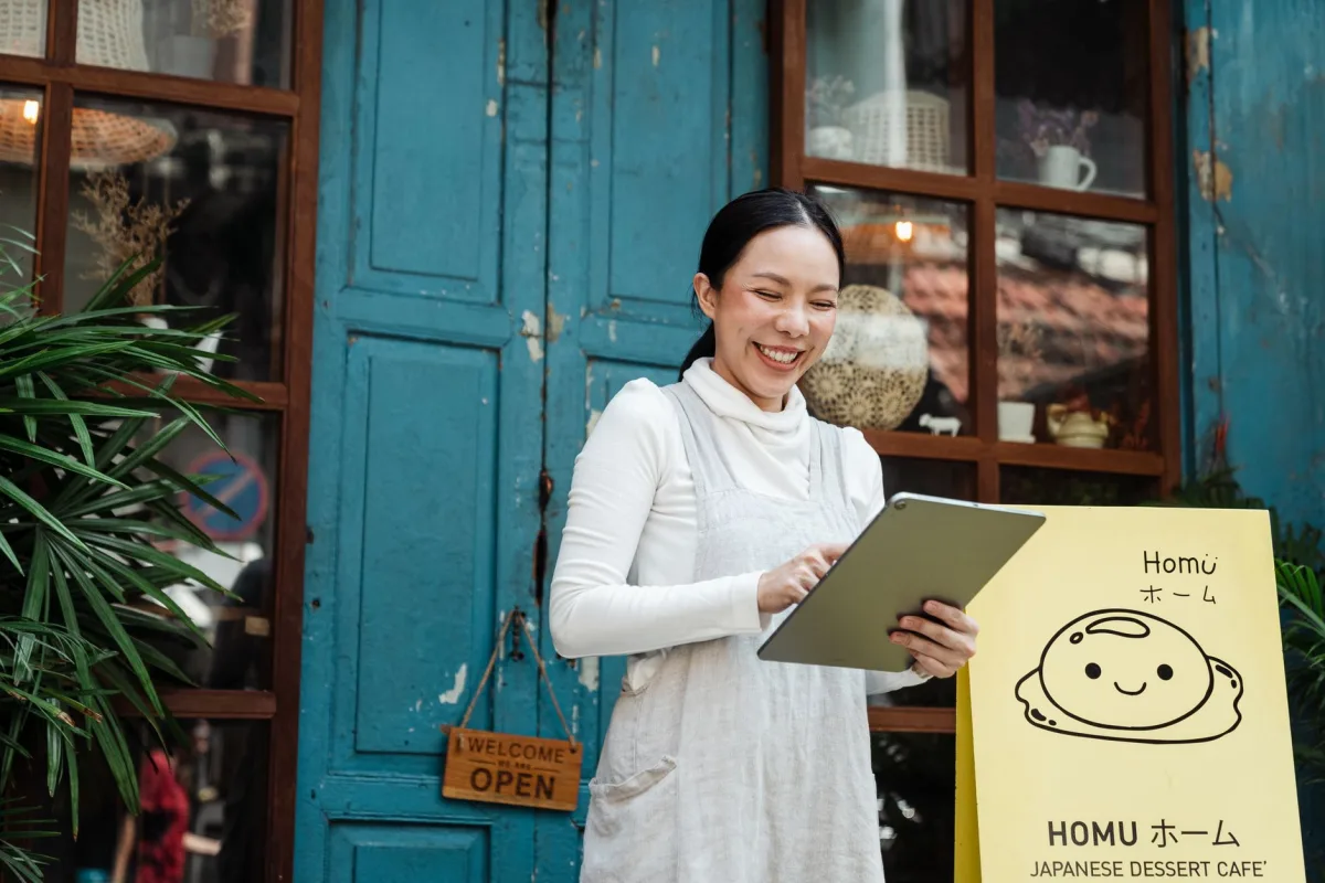 Happy smiling Asian female in casual wear using tablet and standing near rural cafe shop entrance with weathered door Happy smiling Asian female in casual wear using tablet and standing near rural cafe shop entrance with weathered door