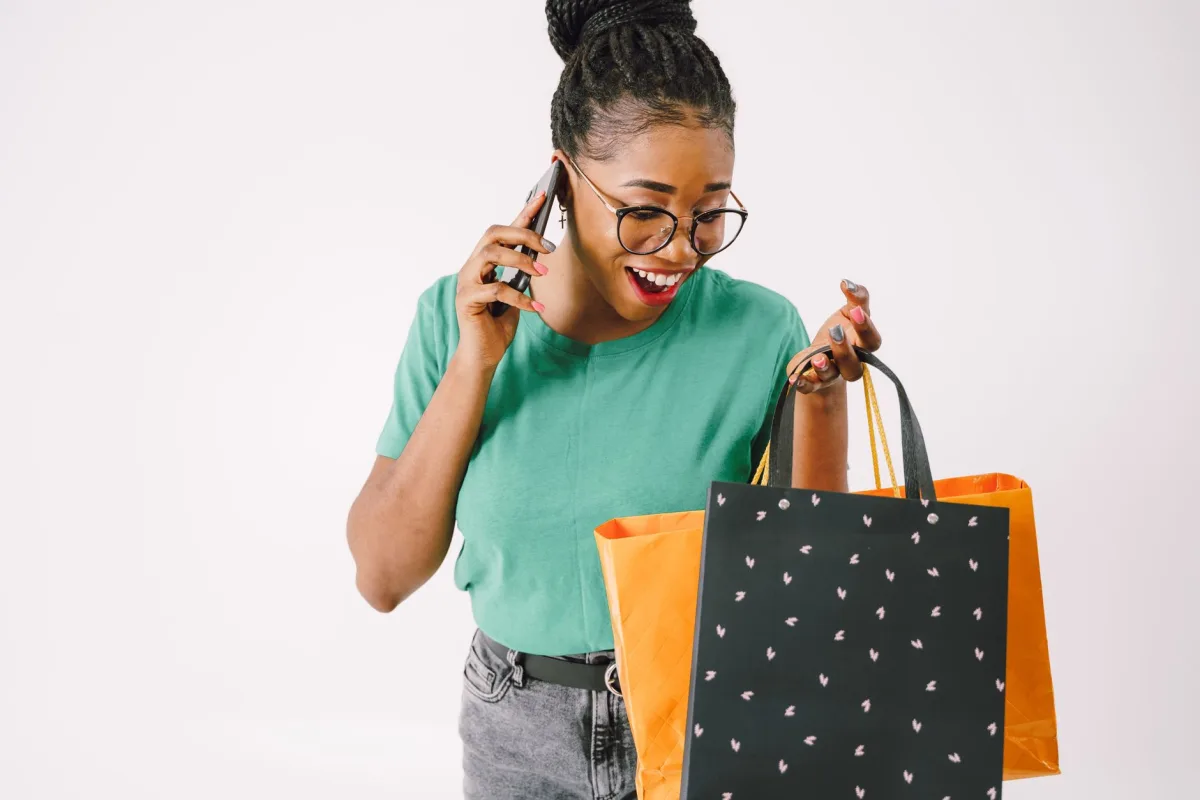 A cheerful woman holding shopping bags and chatting on her phone indoors. A cheerful woman holding shopping bags and chatting on her phone indoors.